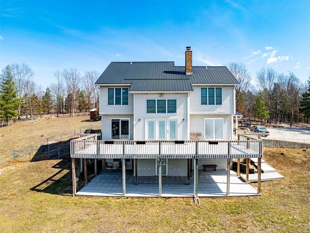 rear view of property with a deck, a chimney, fence, french doors, and a lawn