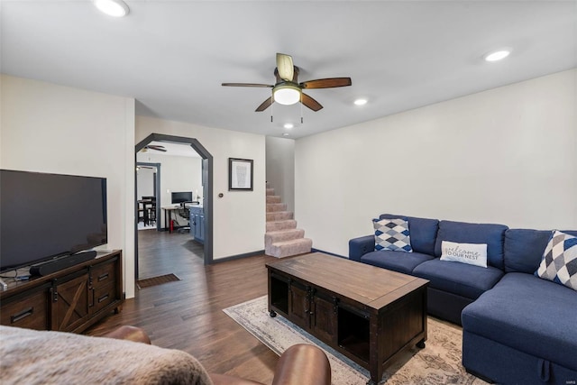 living area with arched walkways, a ceiling fan, recessed lighting, wood finished floors, and stairway