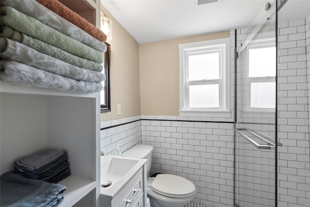 full bath featuring vanity, toilet, a wainscoted wall, tile walls, and tiled shower