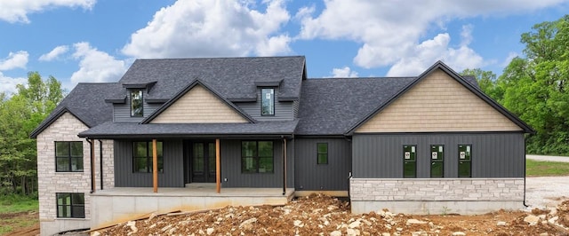 view of front of house featuring roof with shingles, a porch, and stone siding
