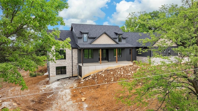 view of front of house with a shingled roof, covered porch, and stone siding