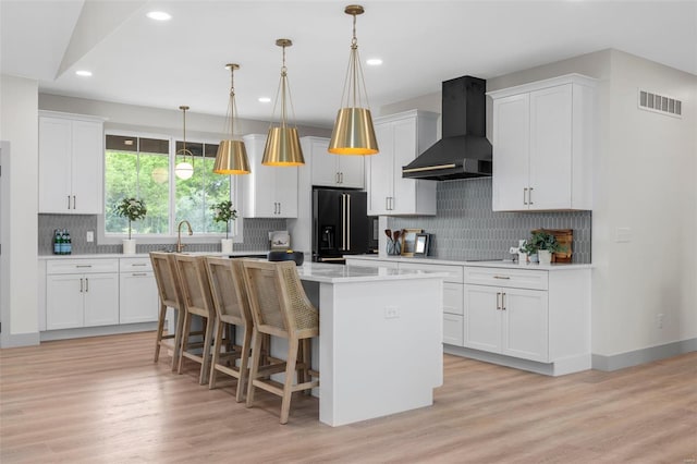 kitchen with black refrigerator with ice dispenser, wall chimney exhaust hood, backsplash, a kitchen island, and visible vents