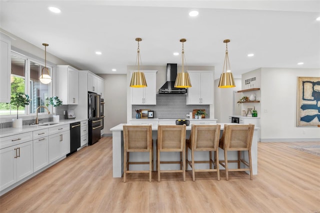 kitchen with wall chimney range hood, a sink, decorative backsplash, visible vents, and black appliances