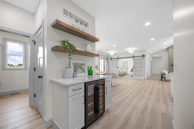 bar featuring light wood-style floors, a barn door, wine cooler, and a wealth of natural light