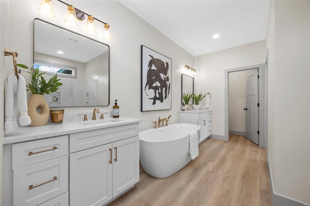 full bath featuring a freestanding tub, a shower, wood finished floors, two vanities, and a sink