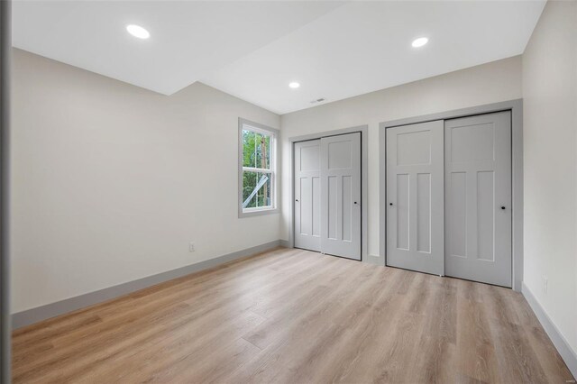 unfurnished bedroom featuring light wood-style floors, recessed lighting, baseboards, and two closets