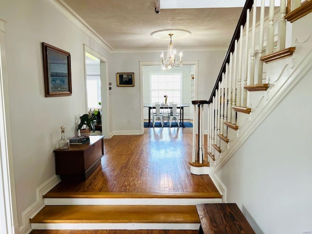 foyer entrance with wood finished floors, an inviting chandelier, stairs, and crown molding