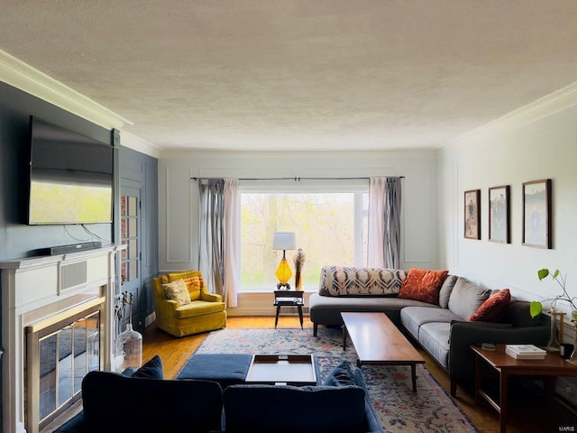 living room with a glass covered fireplace, wood finished floors, a textured ceiling, and ornamental molding