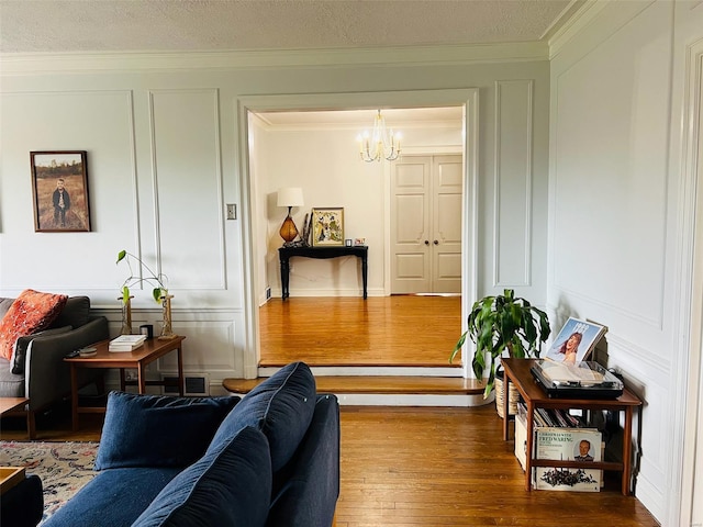 living room with a textured ceiling, an inviting chandelier, a decorative wall, hardwood / wood-style floors, and ornamental molding