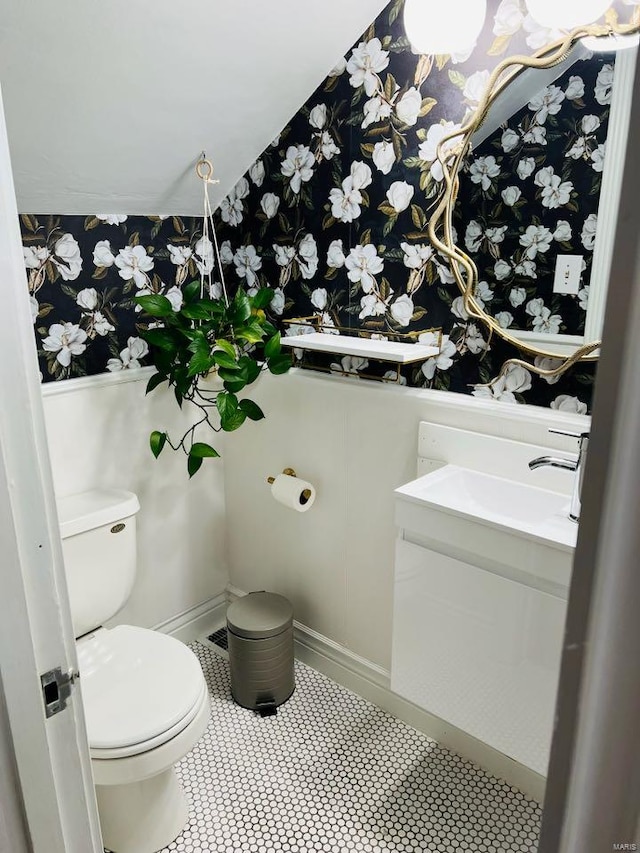 bathroom with toilet, vanity, and wallpapered walls