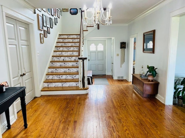 entrance foyer with stairway, hardwood / wood-style floors, visible vents, ornamental molding, and a chandelier