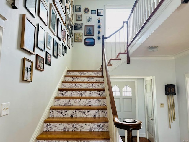 staircase featuring baseboards, a towering ceiling, and crown molding