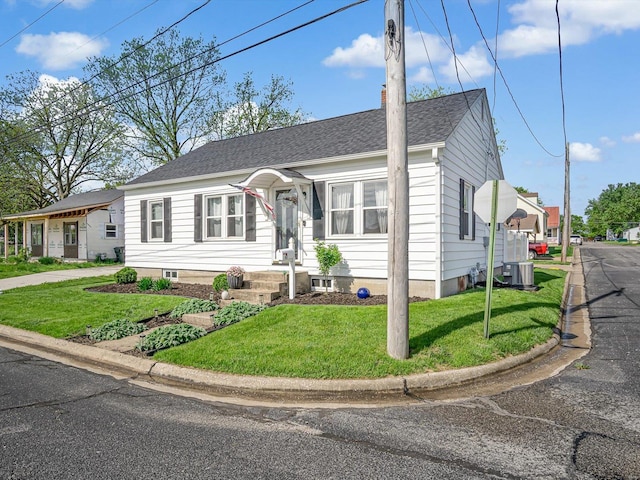 view of front of home featuring roof with shingles, cooling unit, a chimney, and a front yard