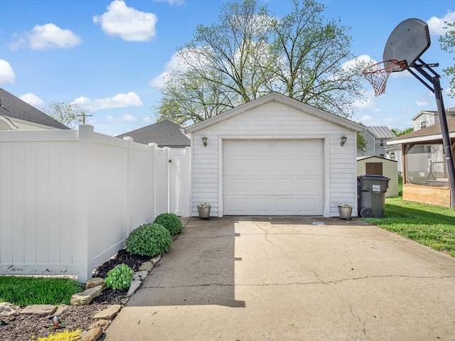 detached garage featuring a storage unit, fence, and concrete driveway