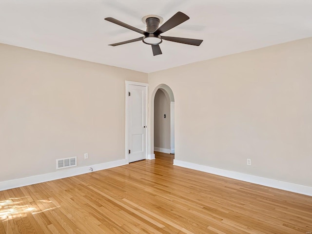 spare room with visible vents, baseboards, light wood-style floors, ceiling fan, and arched walkways