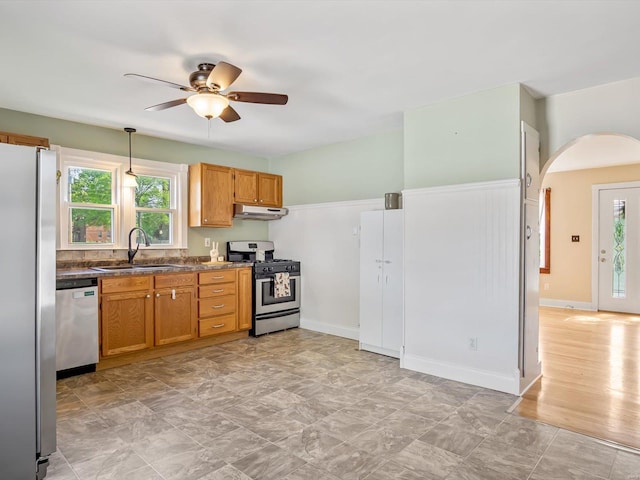 kitchen with appliances with stainless steel finishes, a sink, arched walkways, a ceiling fan, and under cabinet range hood