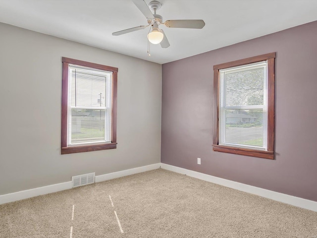 carpeted empty room with baseboards, a ceiling fan, and visible vents