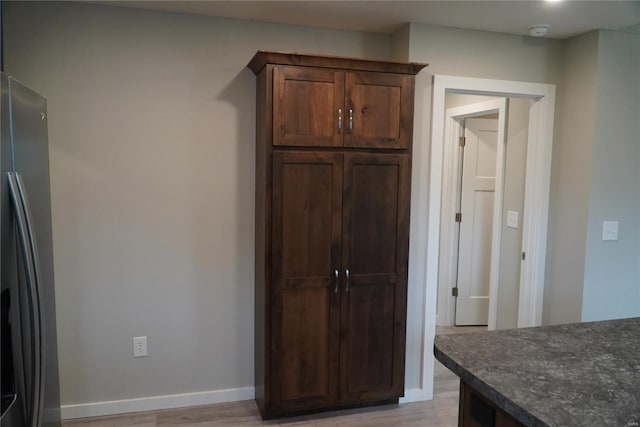 interior space featuring stainless steel refrigerator with ice dispenser, dark stone counters, light wood finished floors, and baseboards