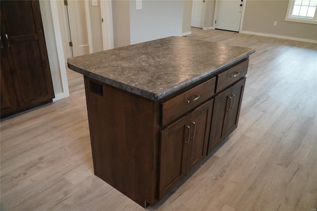 kitchen featuring light wood-style floors, dark countertops, baseboards, and a center island
