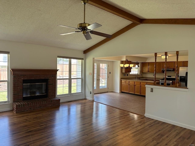 unfurnished living room with ceiling fan with notable chandelier, dark wood finished floors, beam ceiling, and a wealth of natural light