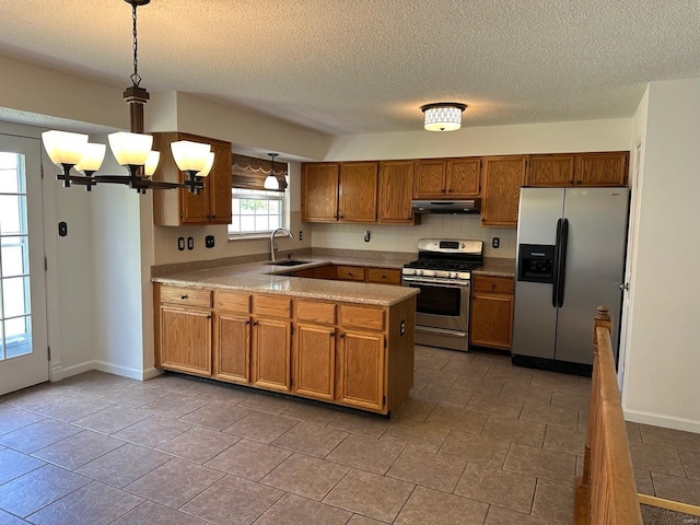 kitchen featuring brown cabinets, appliances with stainless steel finishes, a sink, a peninsula, and under cabinet range hood