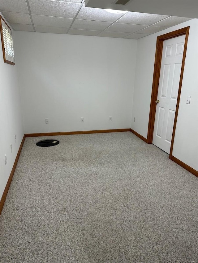 empty room with baseboards, a drop ceiling, and light carpet