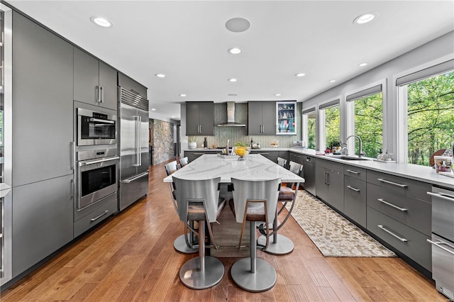 kitchen featuring recessed lighting, a sink, appliances with stainless steel finishes, and wall chimney range hood