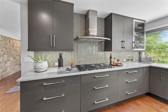 kitchen with backsplash, stainless steel gas stovetop, gray cabinets, and wall chimney exhaust hood