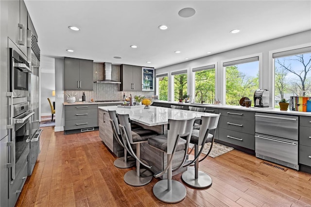 kitchen with recessed lighting, wall chimney exhaust hood, a wealth of natural light, and gray cabinetry