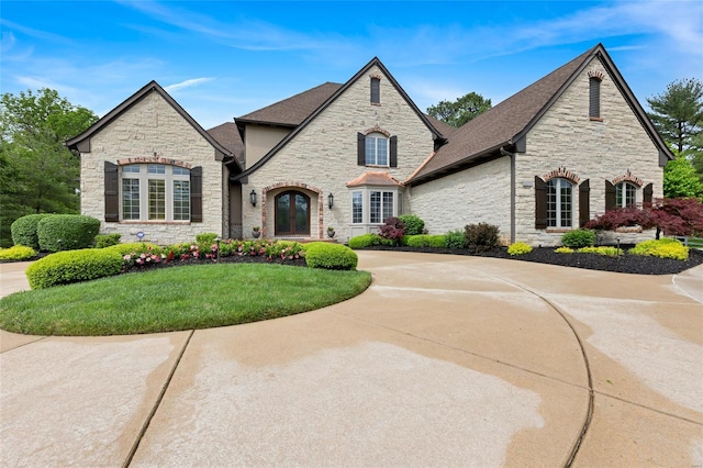 french country inspired facade featuring a shingled roof, a front yard, and stone siding