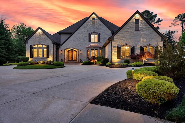 french provincial home with curved driveway and stone siding