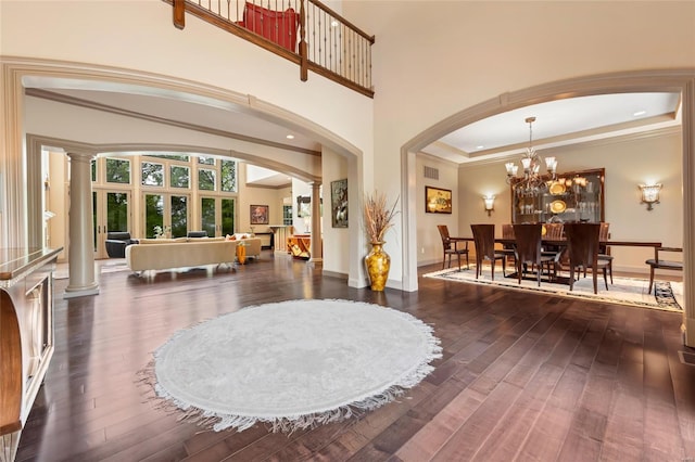 entryway with wood-type flooring, visible vents, decorative columns, an inviting chandelier, and arched walkways