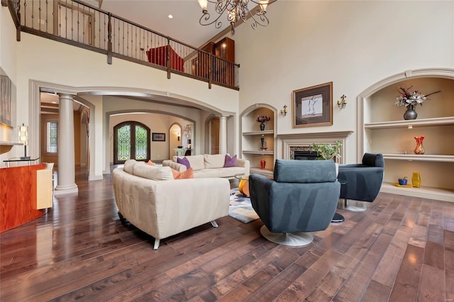 living area with a high ceiling, arched walkways, built in shelves, hardwood / wood-style floors, and decorative columns