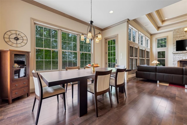 dining space with ornamental molding, dark wood-style flooring, a stone fireplace, and a notable chandelier
