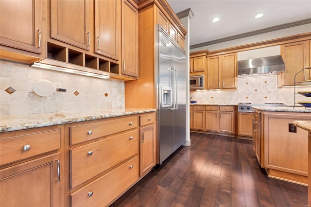 kitchen with ornamental molding, dark wood finished floors, built in appliances, and wall chimney range hood