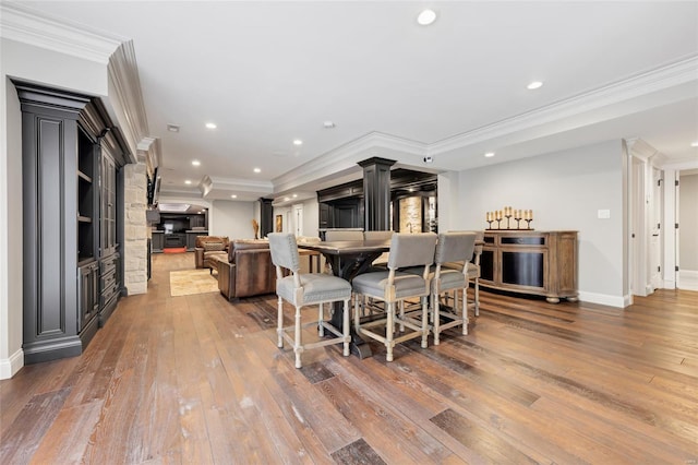 dining space featuring ornamental molding, a fireplace, recessed lighting, ornate columns, and hardwood / wood-style flooring