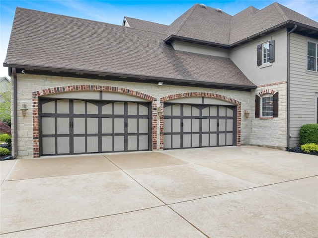 view of front facade featuring concrete driveway, an attached garage, a shingled roof, and stone siding