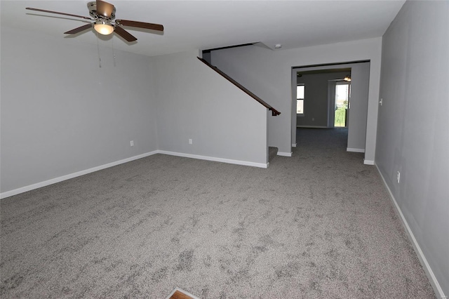 unfurnished living room featuring stairway, ceiling fan, baseboards, and carpet flooring