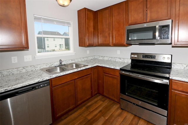 kitchen featuring light stone counters, a sink, brown cabinetry, appliances with stainless steel finishes, and dark wood-style flooring