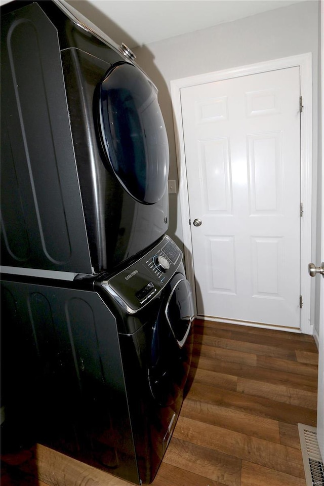 clothes washing area featuring stacked washer / drying machine, wood finished floors, and laundry area