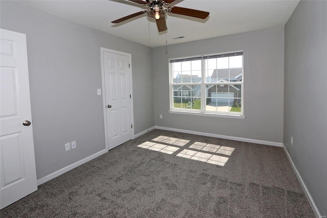 spare room with baseboards, a ceiling fan, visible vents, and dark carpet