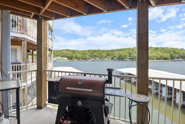 balcony with a water view, a wooded view, and a grill