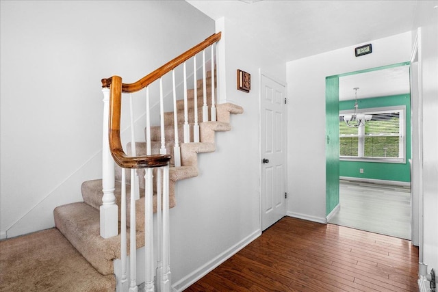 stairway featuring wood finished floors, baseboards, and a notable chandelier