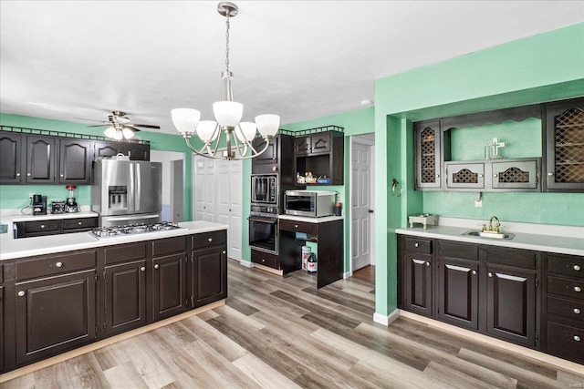kitchen with light countertops, dark brown cabinets, a sink, light wood-style flooring, and appliances with stainless steel finishes