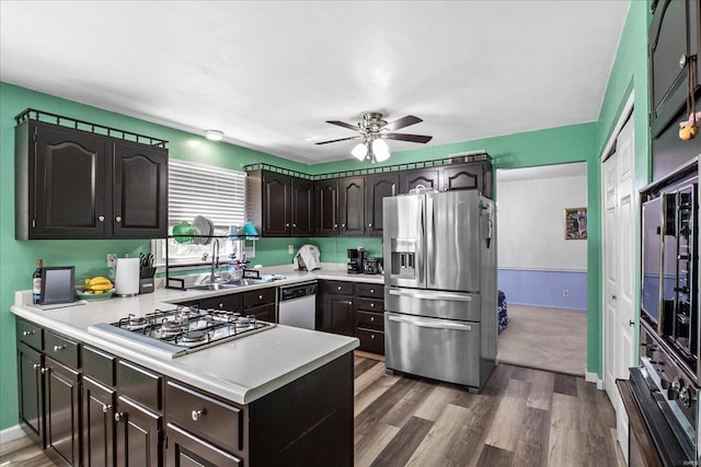 kitchen with stainless steel appliances, light countertops, a ceiling fan, a sink, and a peninsula
