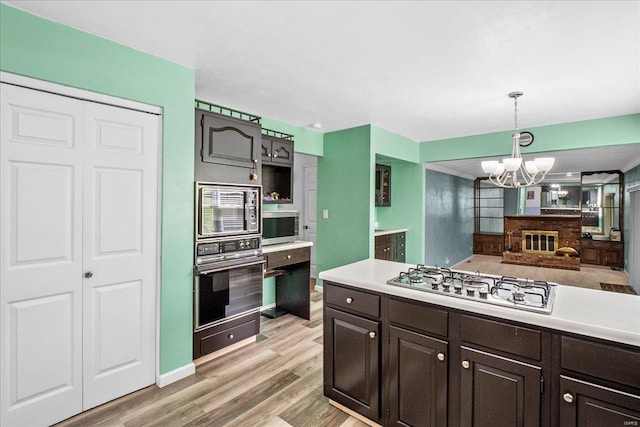 kitchen with dark brown cabinets, an inviting chandelier, stainless steel appliances, light wood finished floors, and light countertops