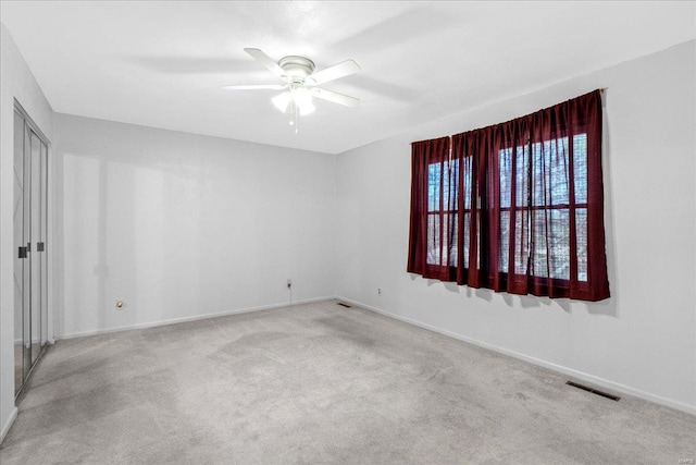 carpeted spare room with baseboards, visible vents, and ceiling fan