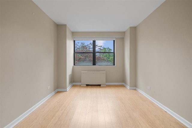 empty room featuring radiator, baseboards, light wood-style flooring, and visible vents
