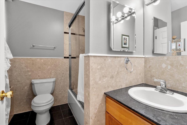bathroom with tile walls, a wainscoted wall, tile patterned floors, toilet, and shower / bath combination with glass door