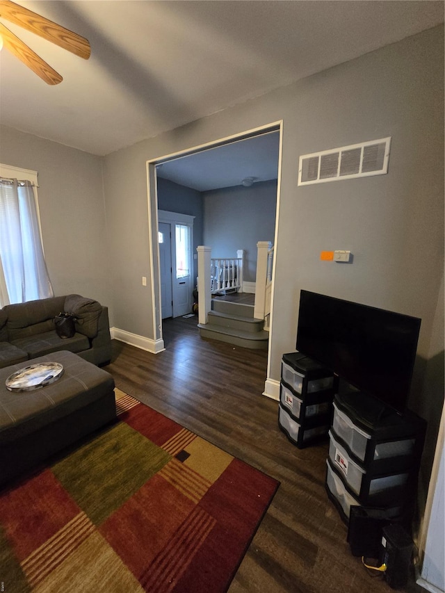 living area featuring stairway, a ceiling fan, visible vents, baseboards, and wood finished floors